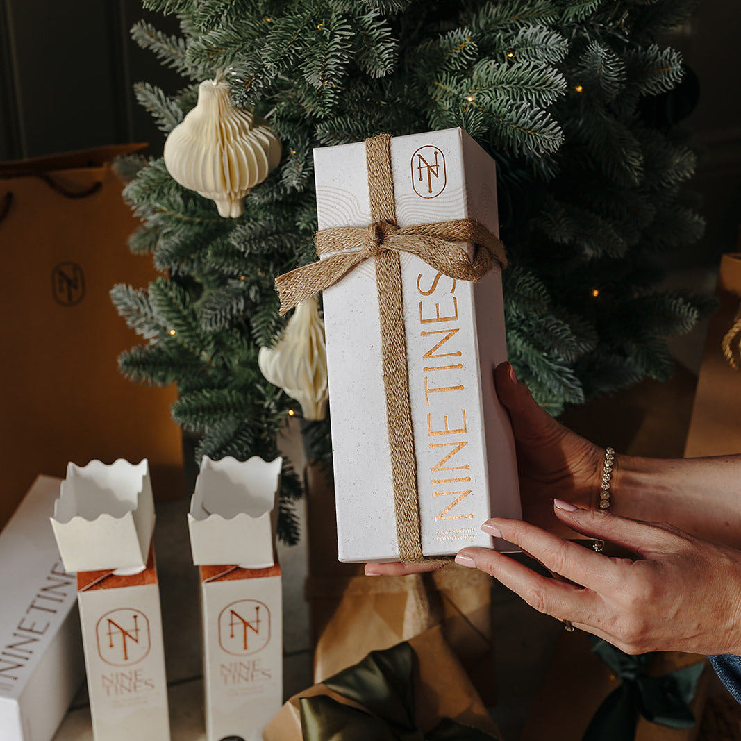 Person holding a  Nine Tines gift box next to a decorated Christmas tree.