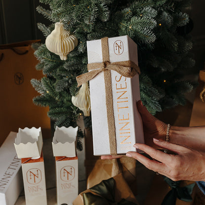 Person holding a  Nine Tines gift box next to a decorated Christmas tree.