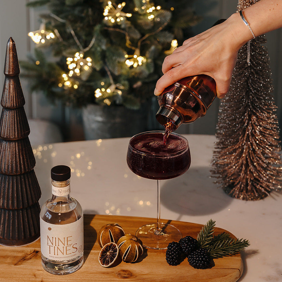 Person pouring a Nine Tines cocktail with Christmas decorations in the background